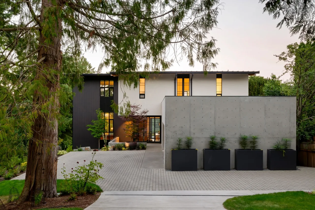 Exterior view of a modern two-story home with black and white siding and a concrete privacy wall with planters in front.