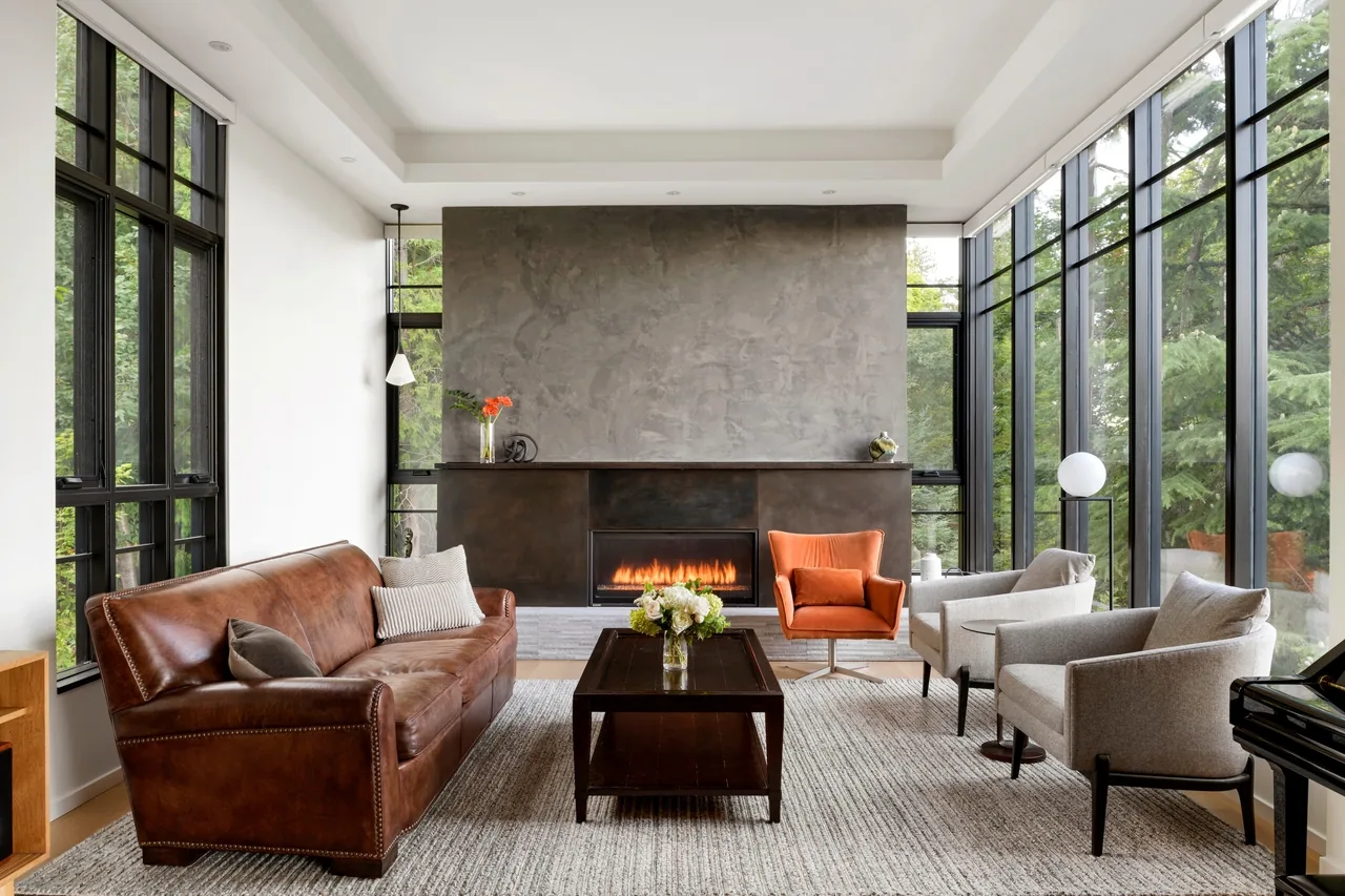 This Sandpoint living room features floor-to-ceiling black window frames and a central fireplace with a minimalist concrete surround.