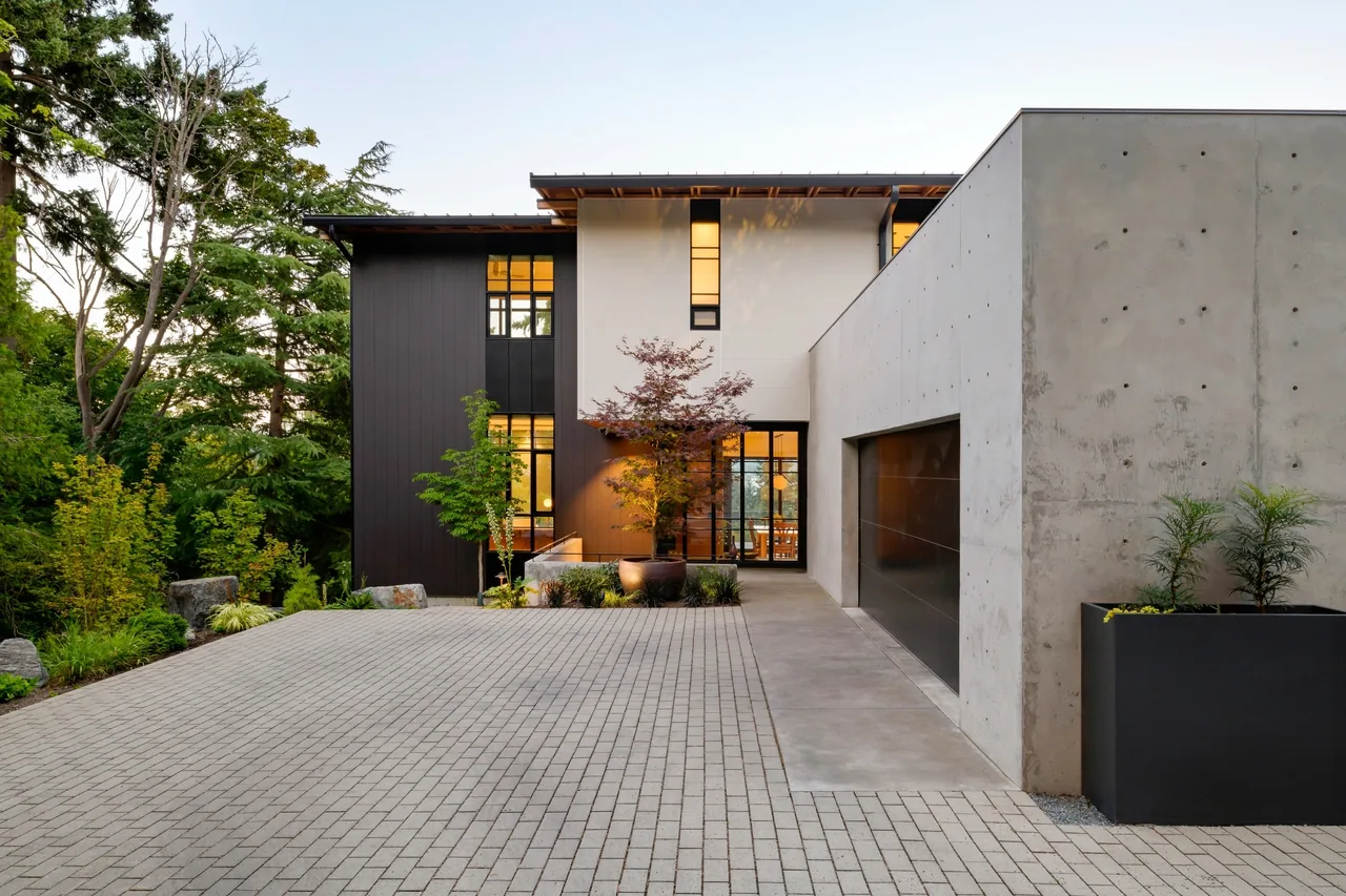 Exterior front view of a modern house with black and white facade, large driveway, and concrete garage wall.