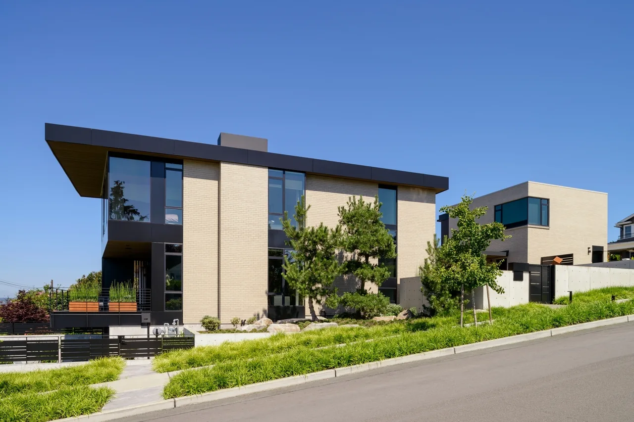 West of Market features a modern residence with beige brick exterior, large black window frames, and flat roof, designed by Sticklab Architecture.