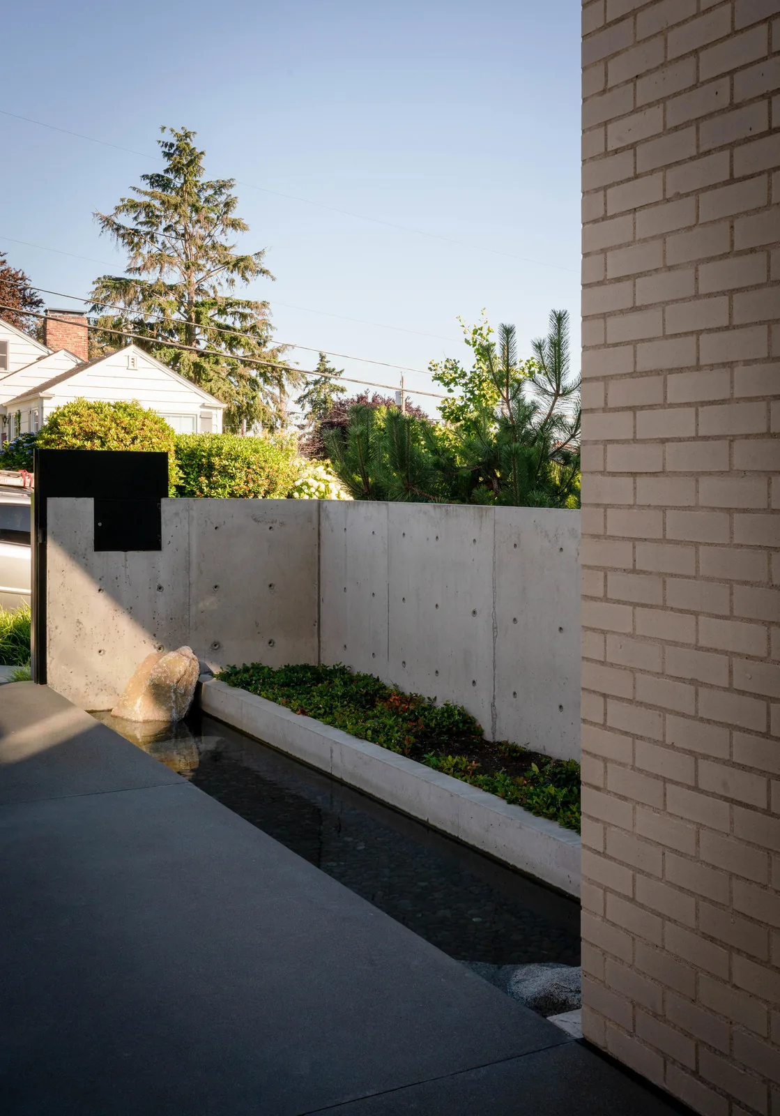 Concrete planter with water and greenery beside a pale brick wall in the West of Market project by Sticklab Architecture.