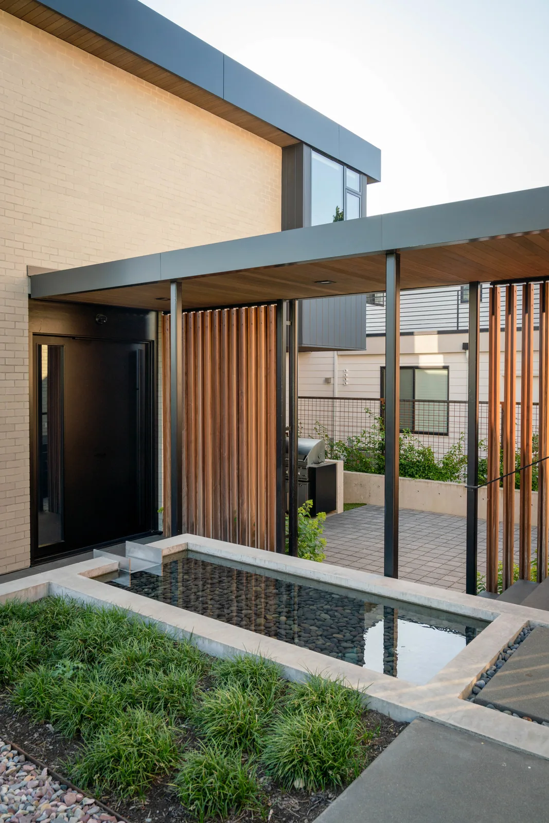 The West of Market project features a reflecting pool by the entry, vertical wood slats, and a covered patio with black metal posts.