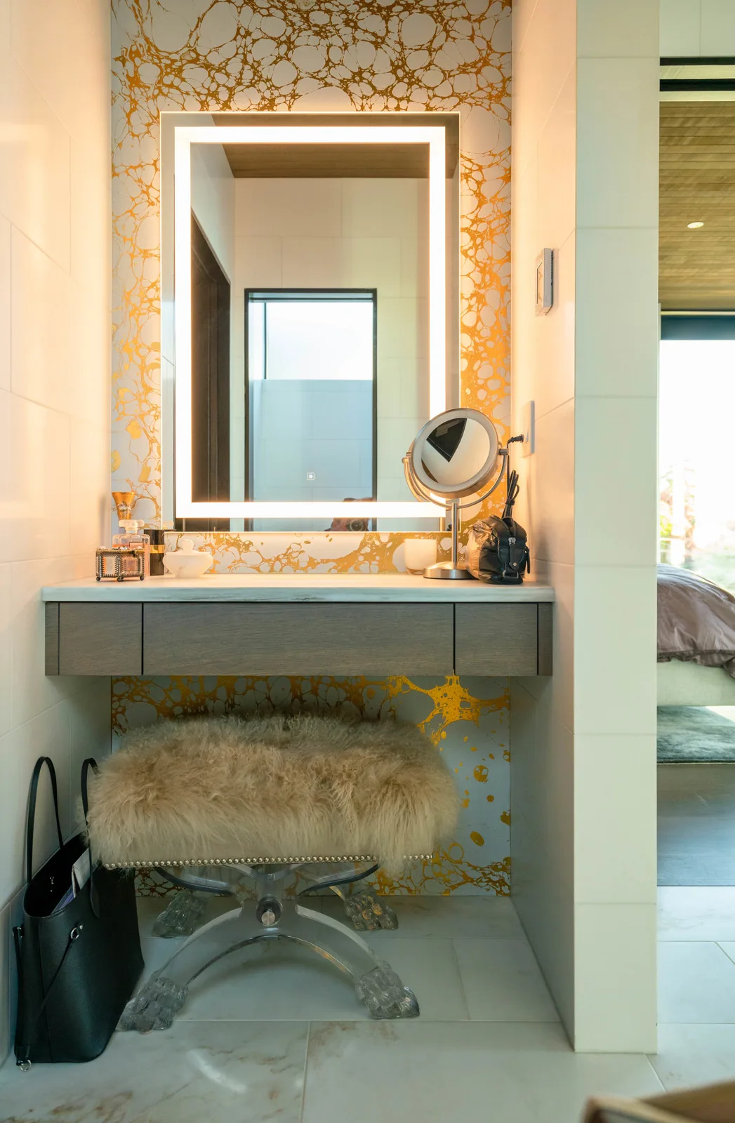 Vanity nook features an illuminated rectangular mirror above a floating wood vanity with a plush furry stool.