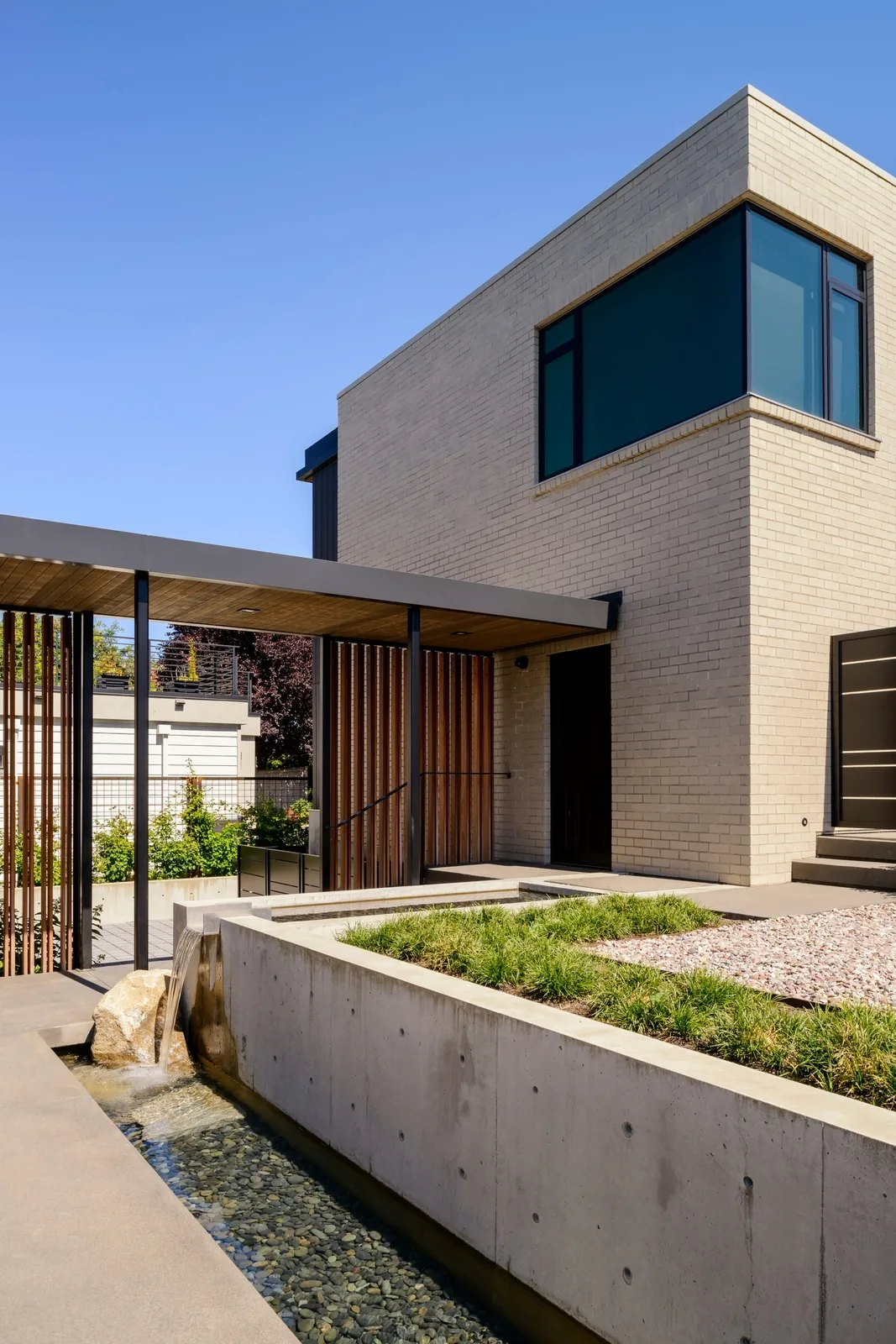 Exterior front view of a modern residence with cream brick walls, large corner windows, and a covered porch with vertical wood slats