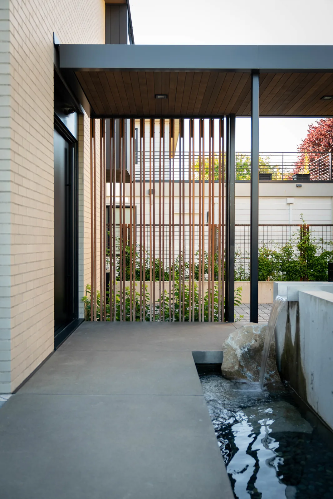 Covered patio area showcasing vertical wooden slats and a concrete reflecting pool with a waterfall feature.