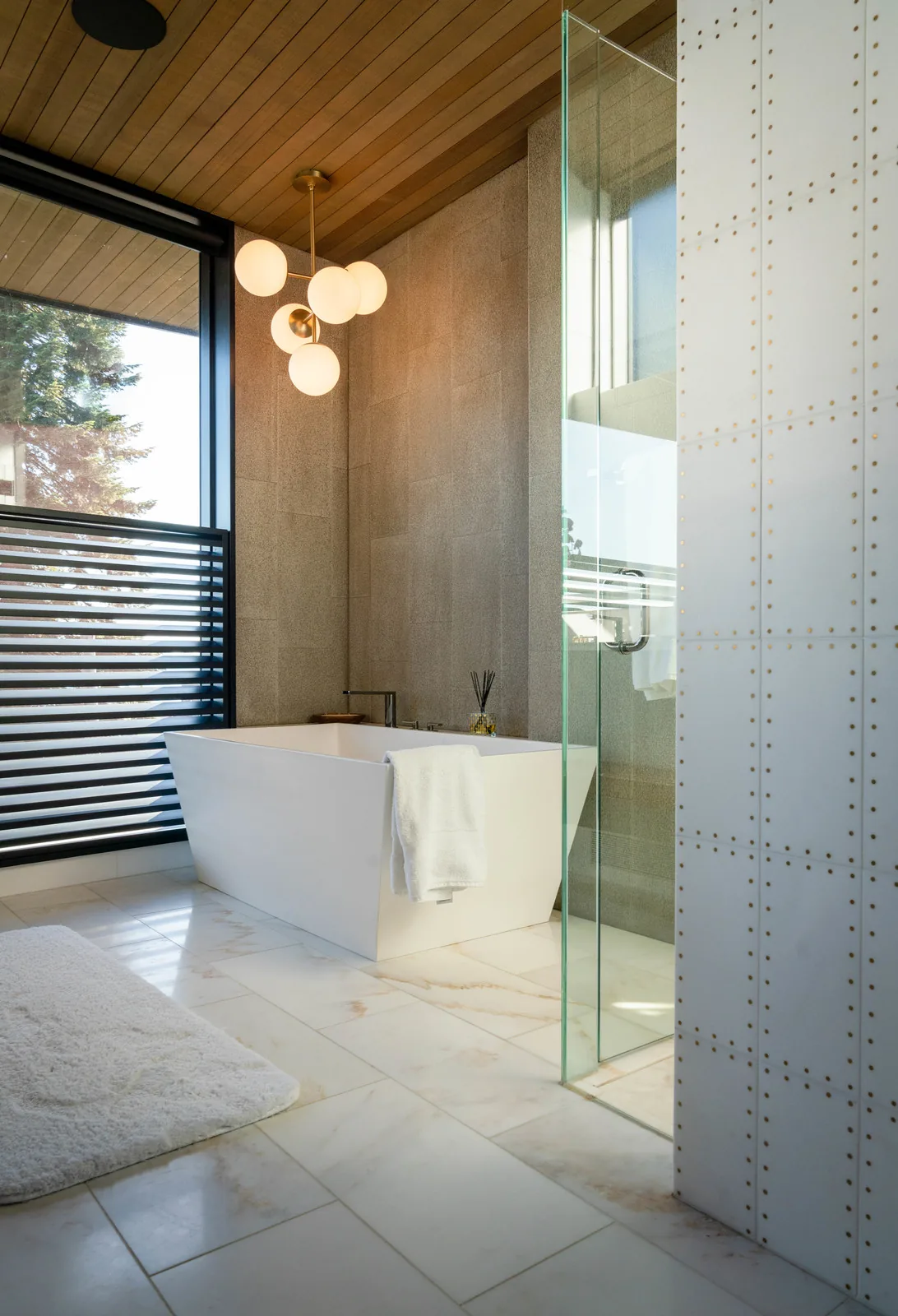 Modern bathroom featuring a freestanding tub, wooden ceiling panels, and a marble floor with natural veining.