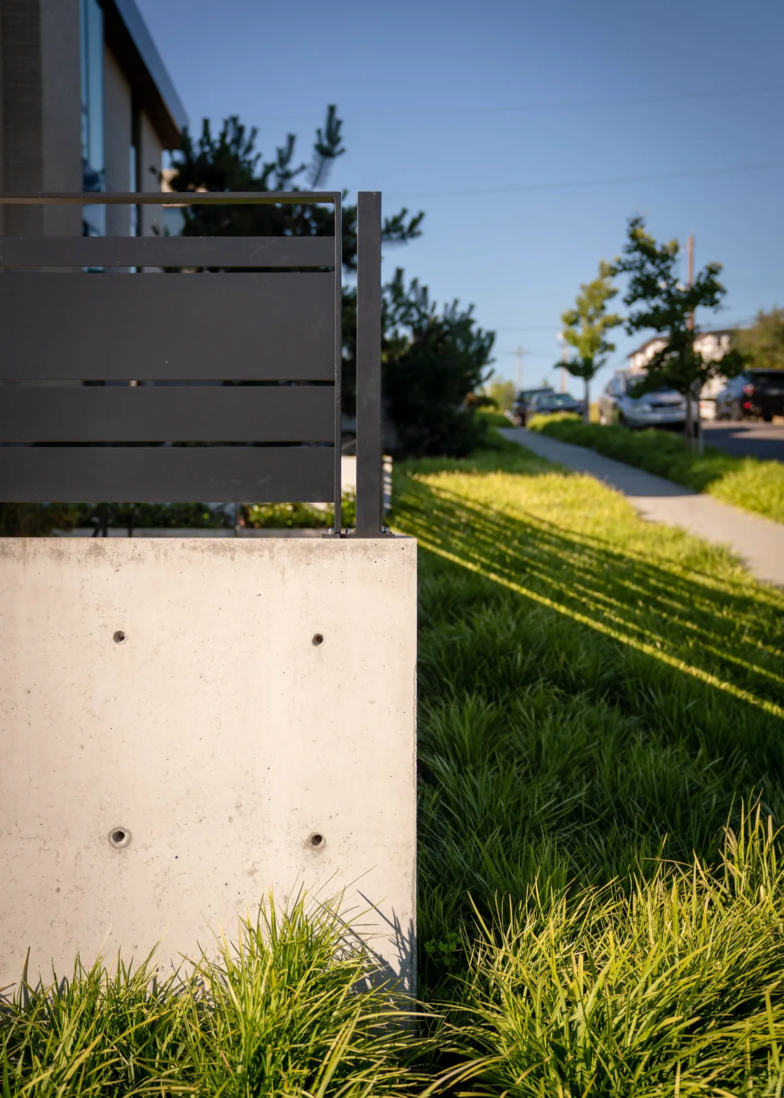A concrete retaining wall with black horizontal metal railing borders landscaped grass beside a sidewalk.