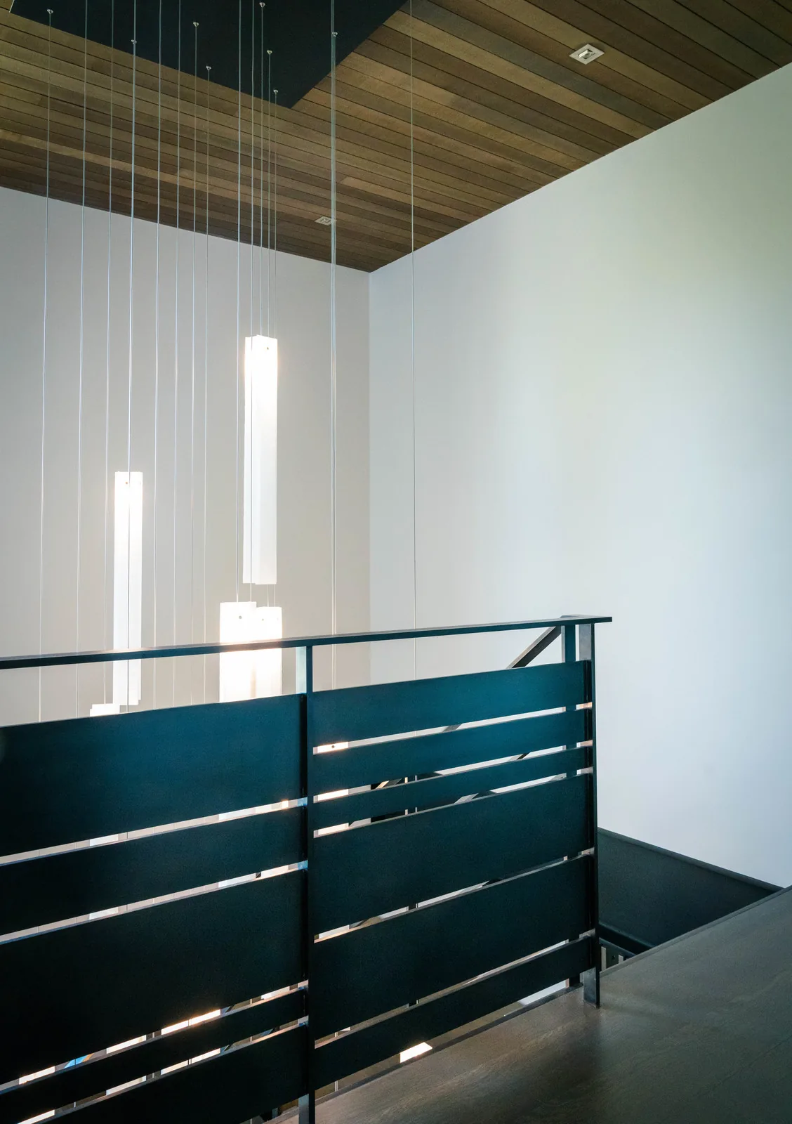 Interior stairway features black metal railings and pendant lighting against white walls and wooden ceiling.