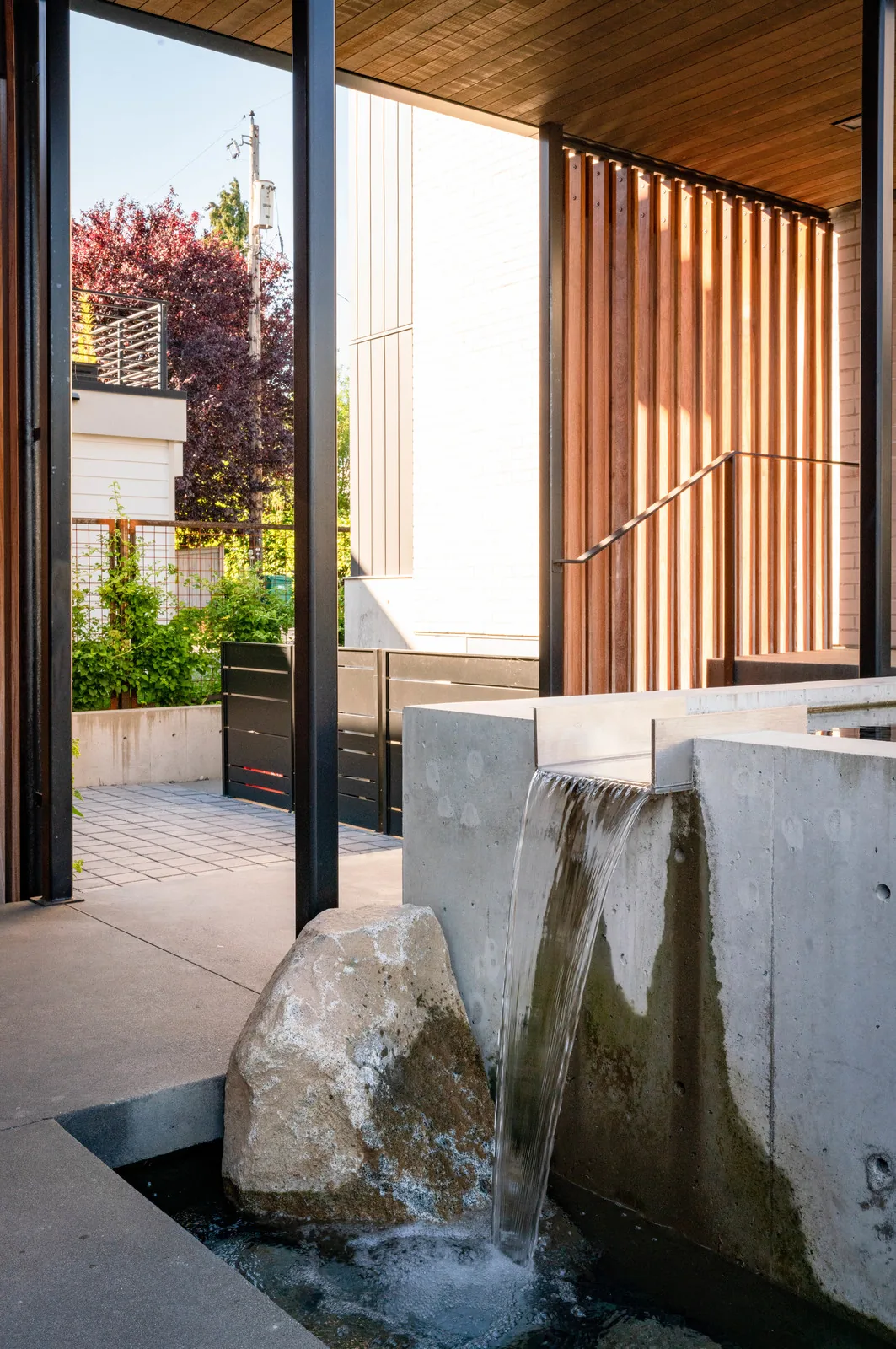A concrete water feature flows next to vertical wooden slats under a wooden ceiling overhang.