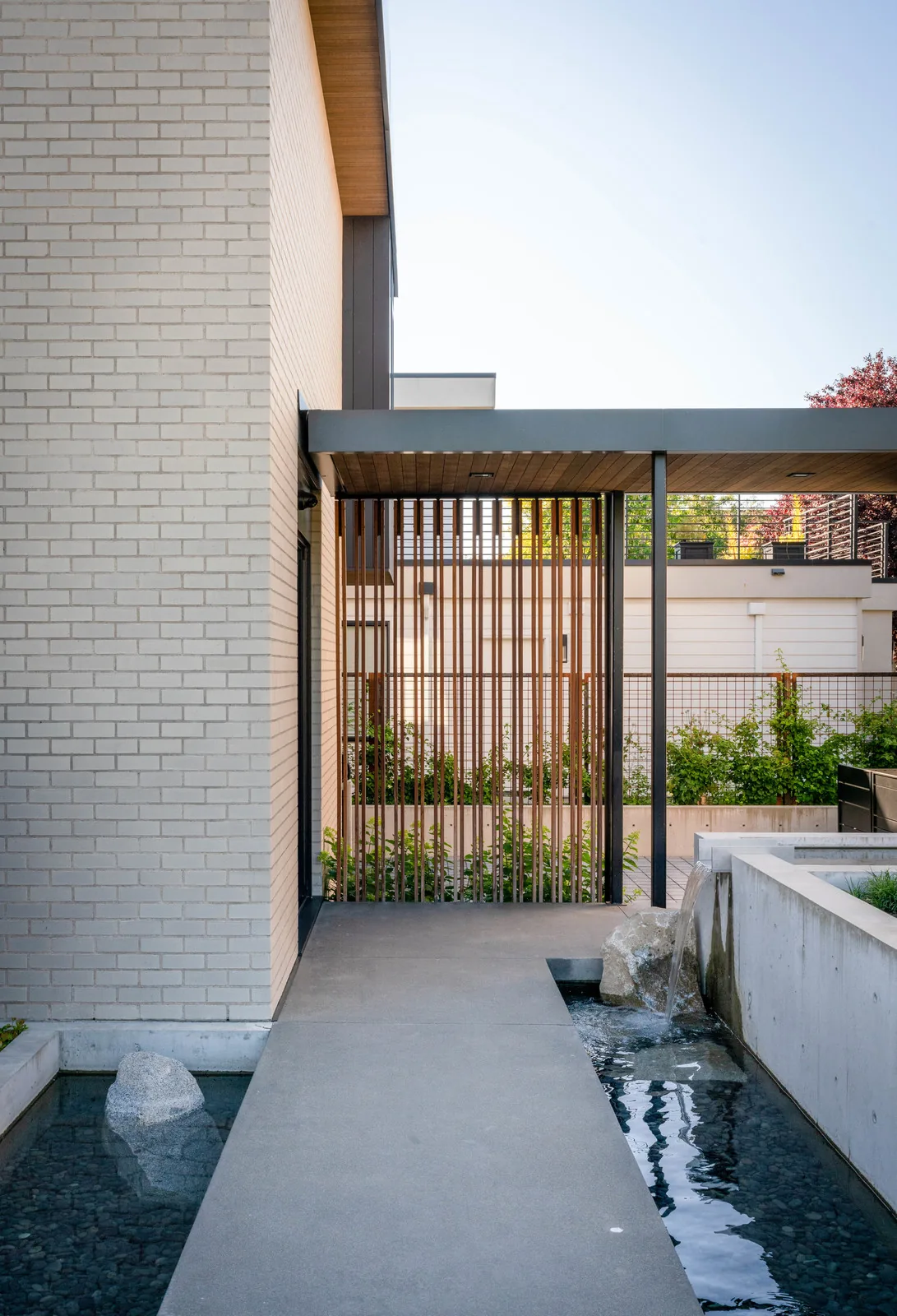 Outdoor entry area with water features, wooden vertical slats, and a flat roof canopy.