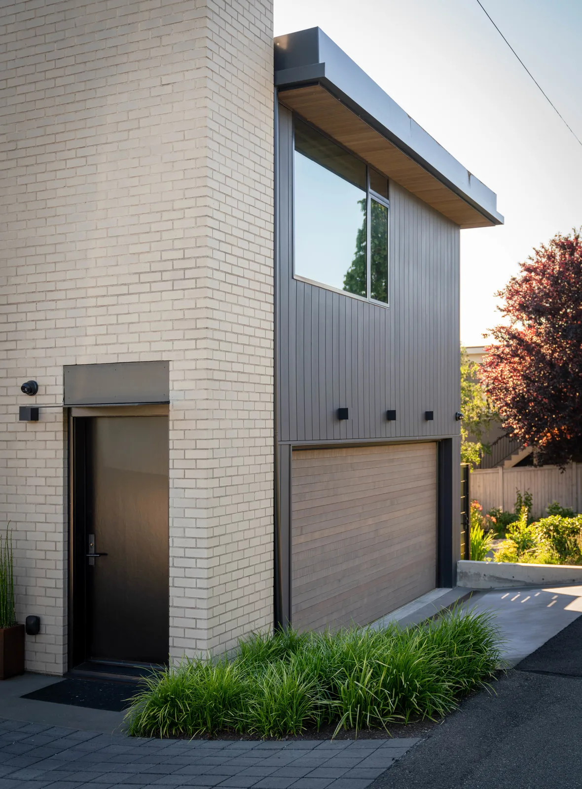 Modern residential exterior with beige brick, vertical siding, and a large upper window over the garage