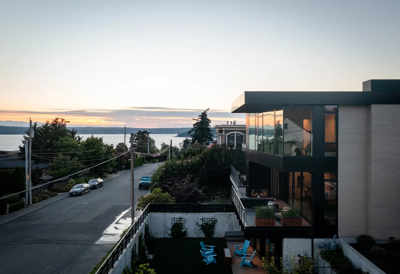 The West of Market project by Sticklab Architecture features floor-to-ceiling glazing and a balcony with seating, capturing waterfront views at sunset.