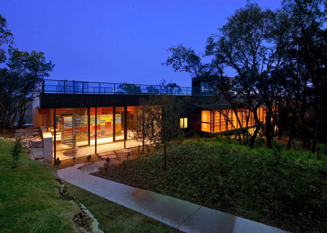 Wimberley Residence by Cunningham Architects, showing the illuminated exterior with floor-to-ceiling glazing and a pathway leading to the entrance.