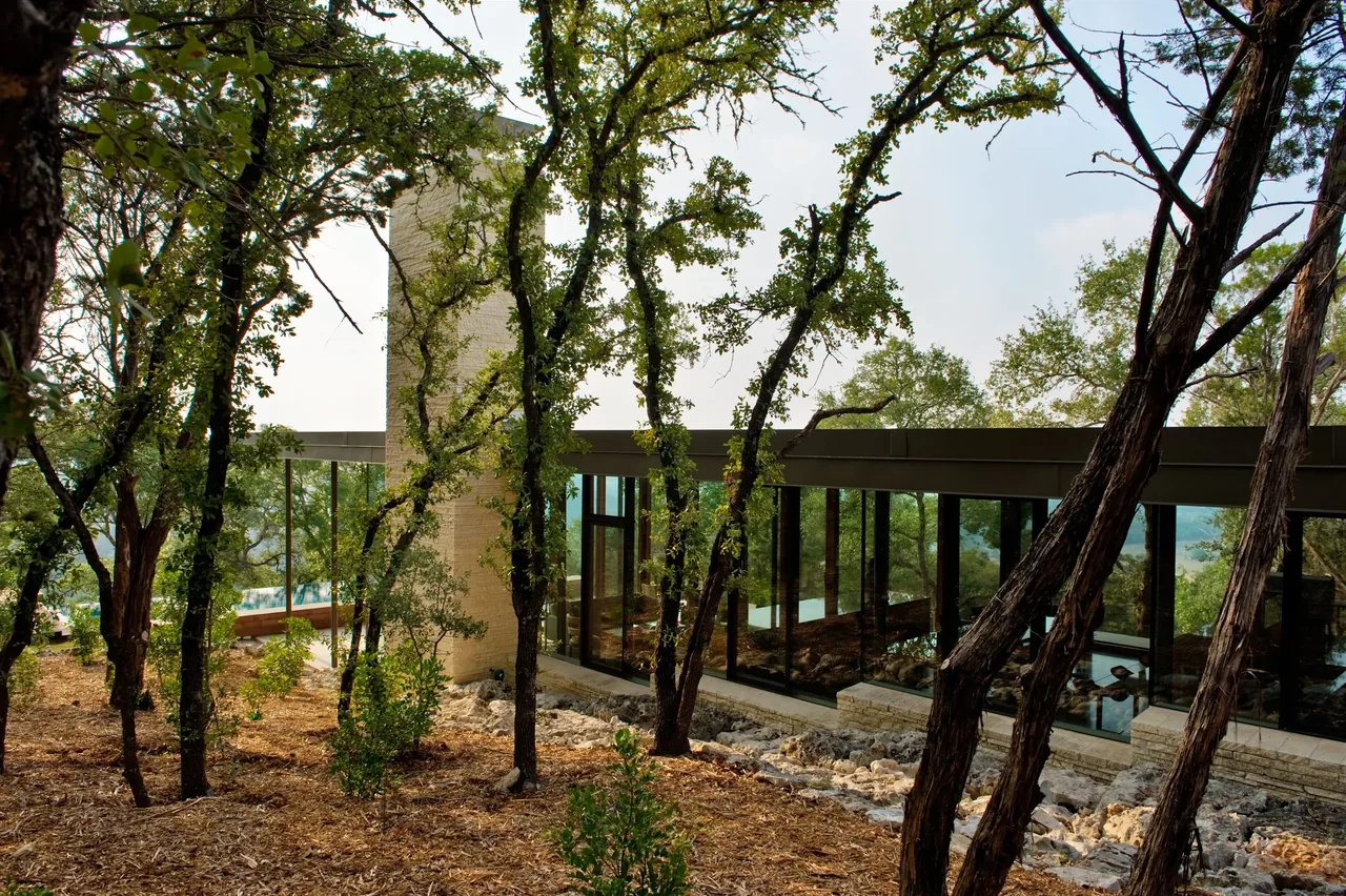 The Wimberley Residence by Cunningham Architects features floor-to-ceiling glass walls and a stone chimney in a forest setting.