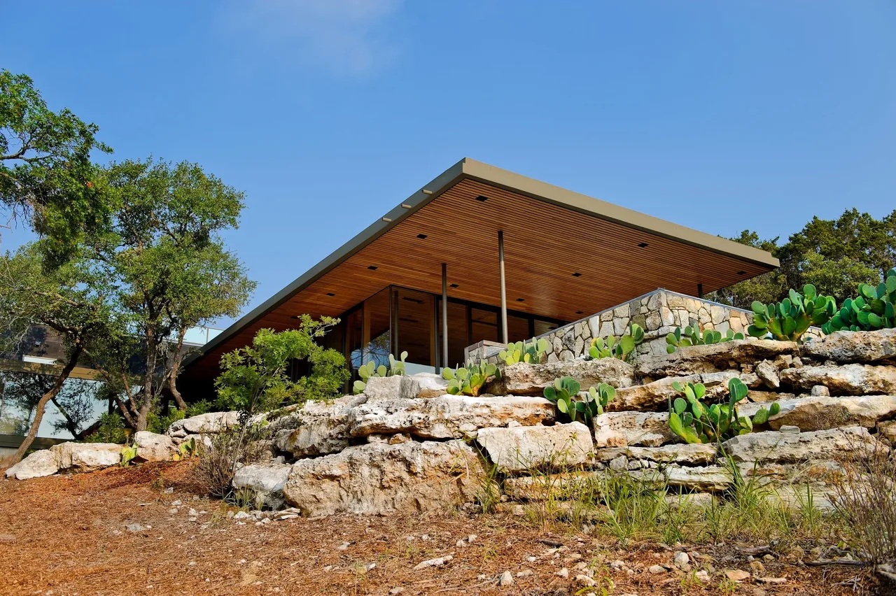 Wimberley Residence by Cunningham Architects features a flat roof and natural stone retaining walls blending with the landscape.