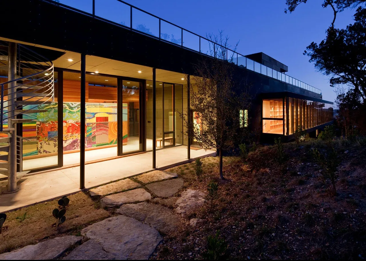 Wimberley Residence by Cunningham Architects features illuminated interiors with visible artwork and a stone chimney element.