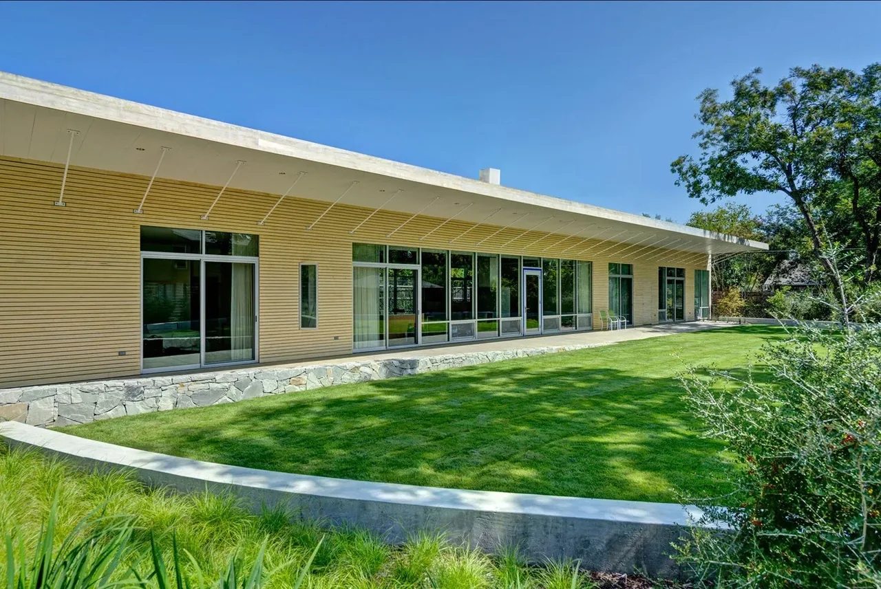 Pomona Residence features a modern style facade with wood siding, extensive glazing, and a stone retaining wall.