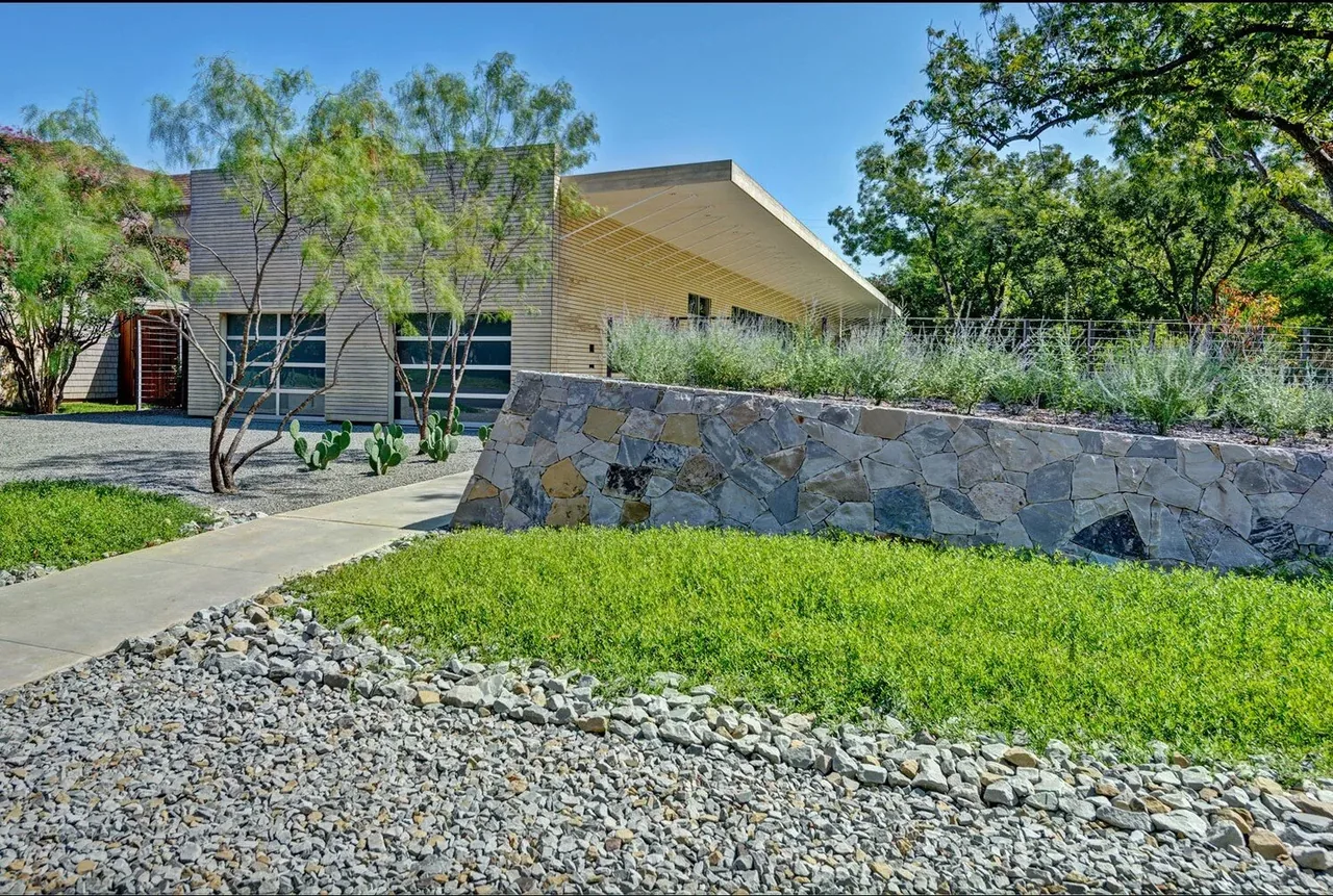 Pomona Residence features a horizontal form with wood siding and a stone retaining wall in the front yard.