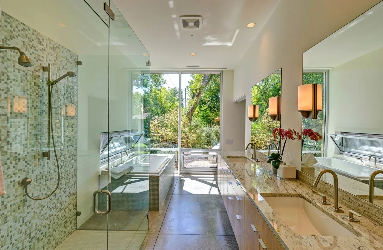 Bathroom with glass-enclosed shower, double vanity, and bathtub by a large window overlooking greenery.