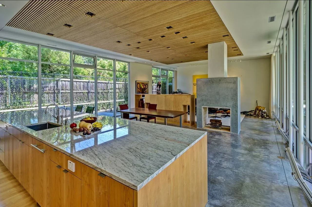 Open kitchen and dining space with a wood slatted ceiling and concrete fireplace at Pomona Residence by Cunningham Architects.
