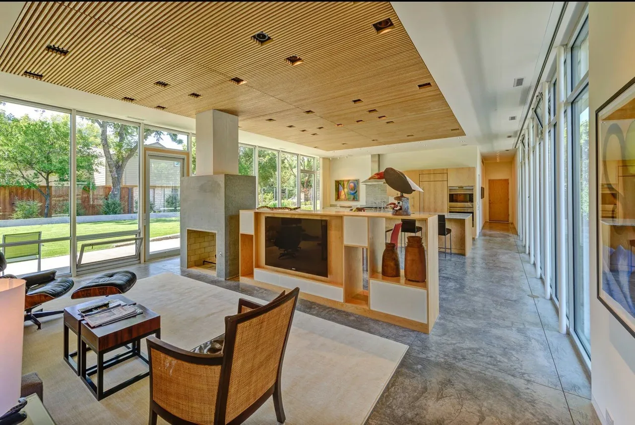 Pomona Residence living and kitchen space flows openly with floor-to-ceiling glazing and a concrete fireplace.