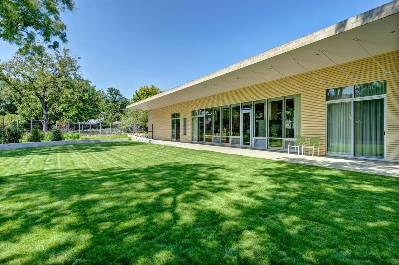 The Pomona Residence features a large lawn with an expansive wall of floor-to-ceiling glass and a wood slatted ceiling overhang.