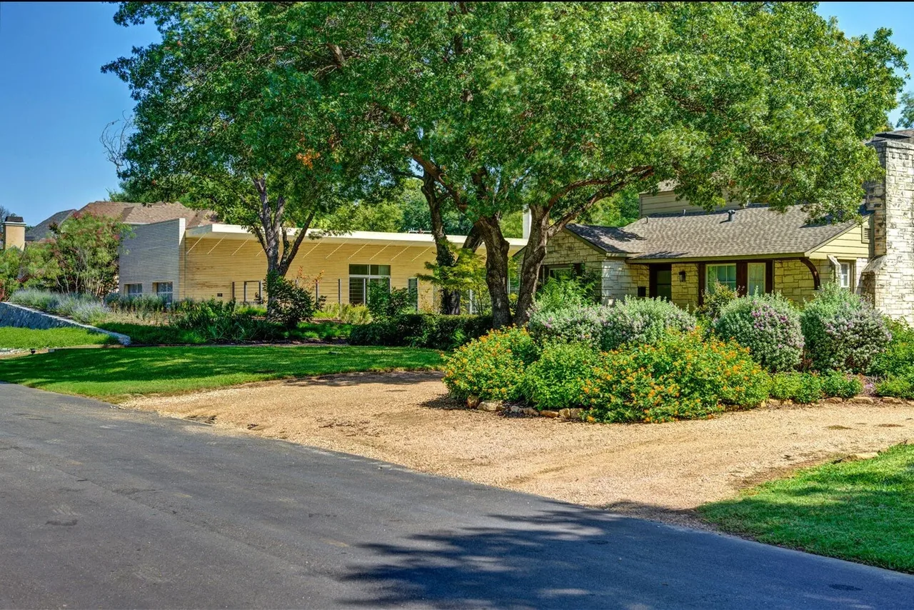Exterior view of two adjacent houses partially obscured by trees and plants under a clear blue sky.