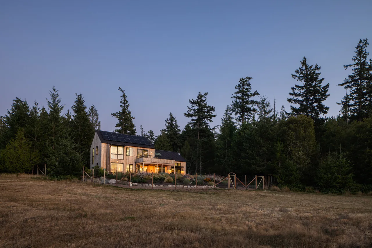 Fisherman Bay Residence by David Vandervort Architects features wood siding and solar panels on a gable roof, set in a rural landscape near Seattle.