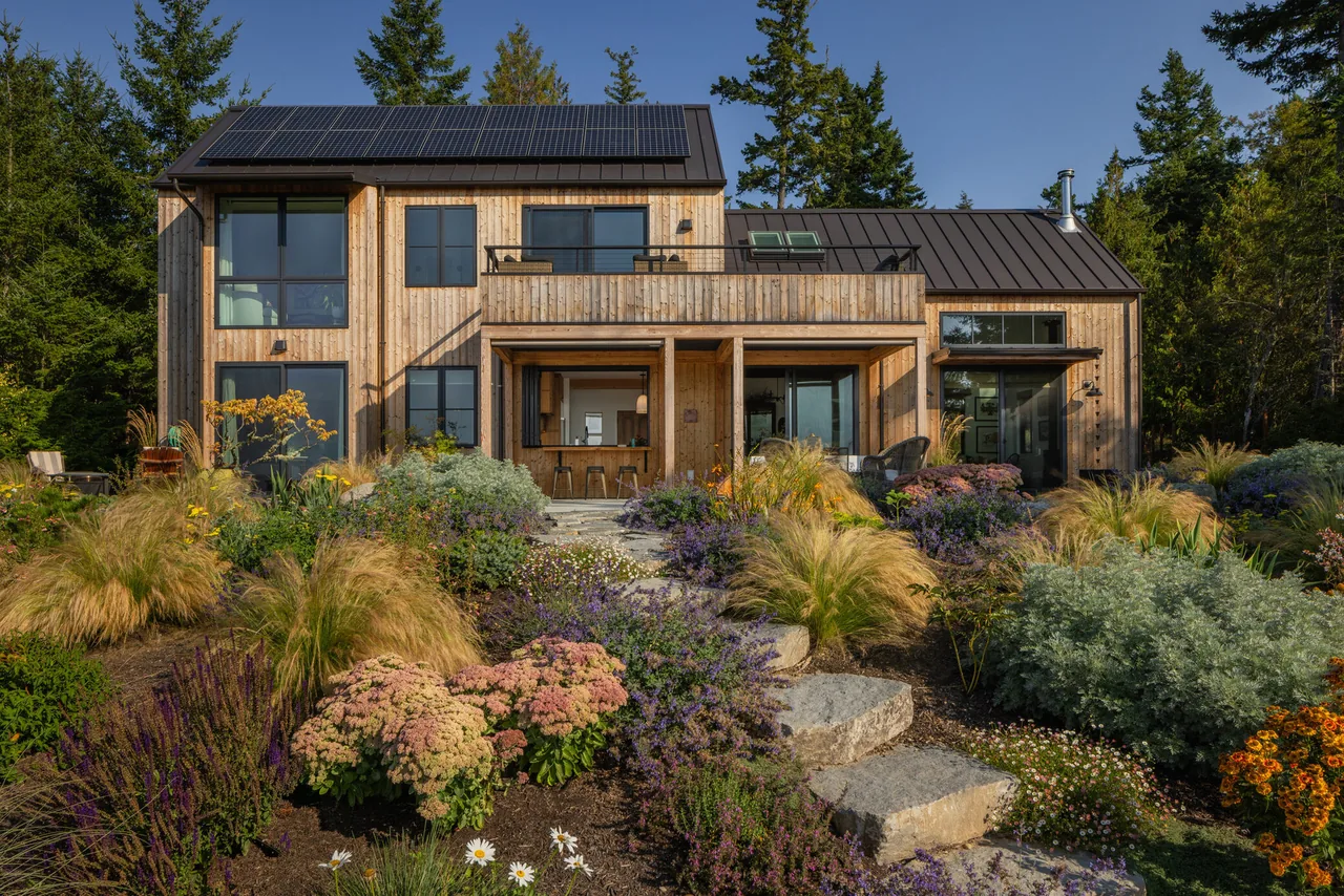 Modern two-story wood siding home with blackened steel standing seam metal roof and solar panels in a rural setting.