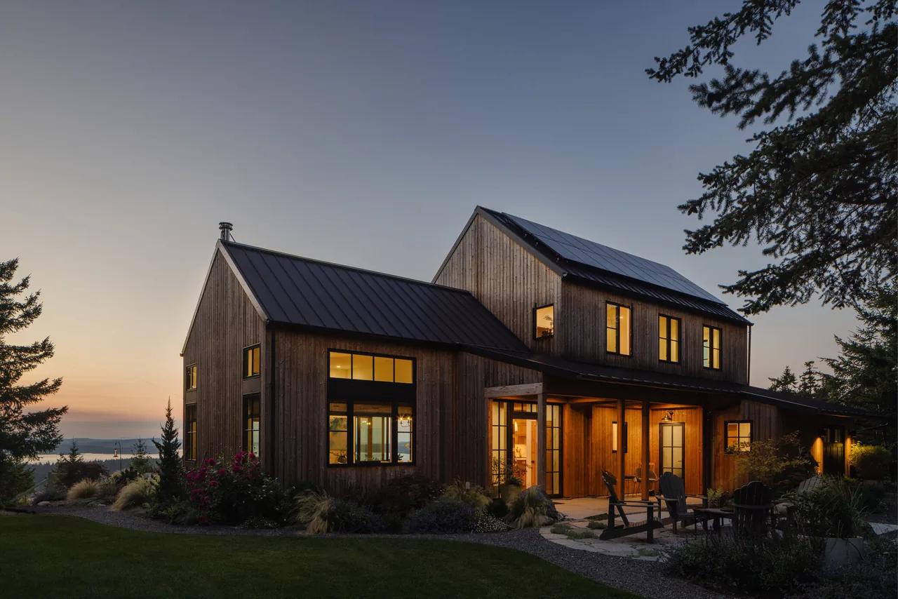 The Fisherman Bay Residence by David Vandervort Architects features a modern farmhouse design with wood siding and metal roofing at dusk.
