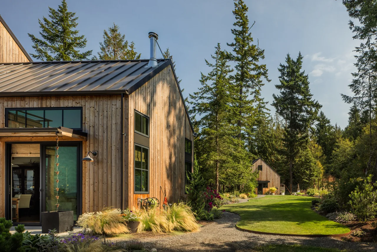 Fisherman Bay Residence features wood siding and a standing seam metal roof in a forested setting.