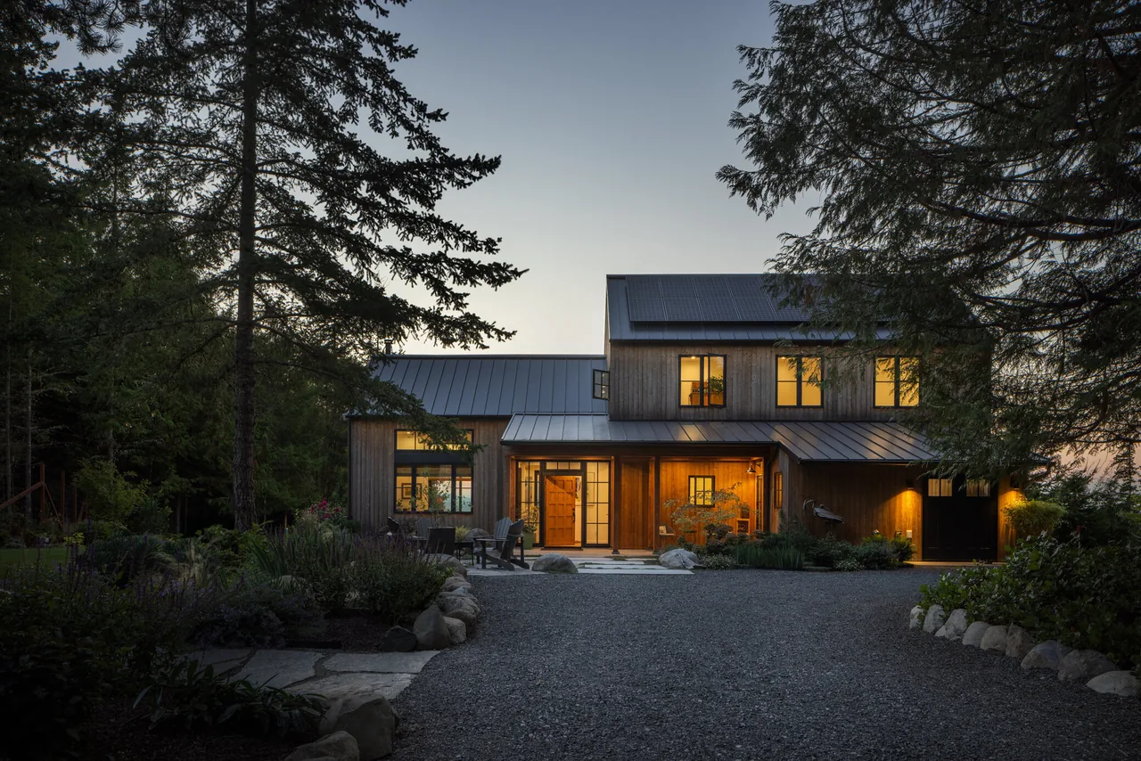 The Fisherman Bay Residence features wood siding and standing seam metal roofs with warm lighting at dusk.