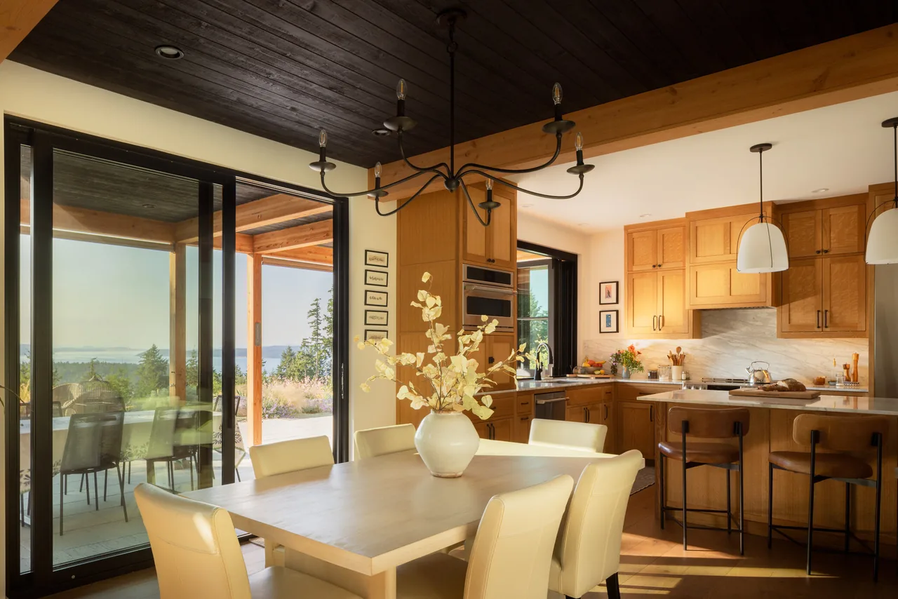 Dining room and kitchen with wood cabinets and ceiling open to a covered patio and scenic outdoor views.