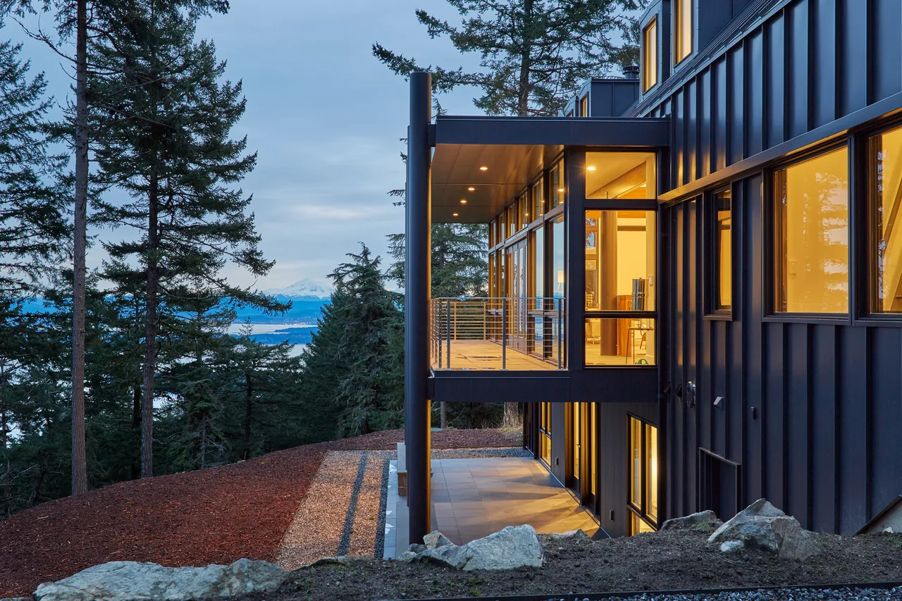 The Buck Mountain Residence features black standing seam metal siding and floor-to-ceiling glazing in a forested setting.