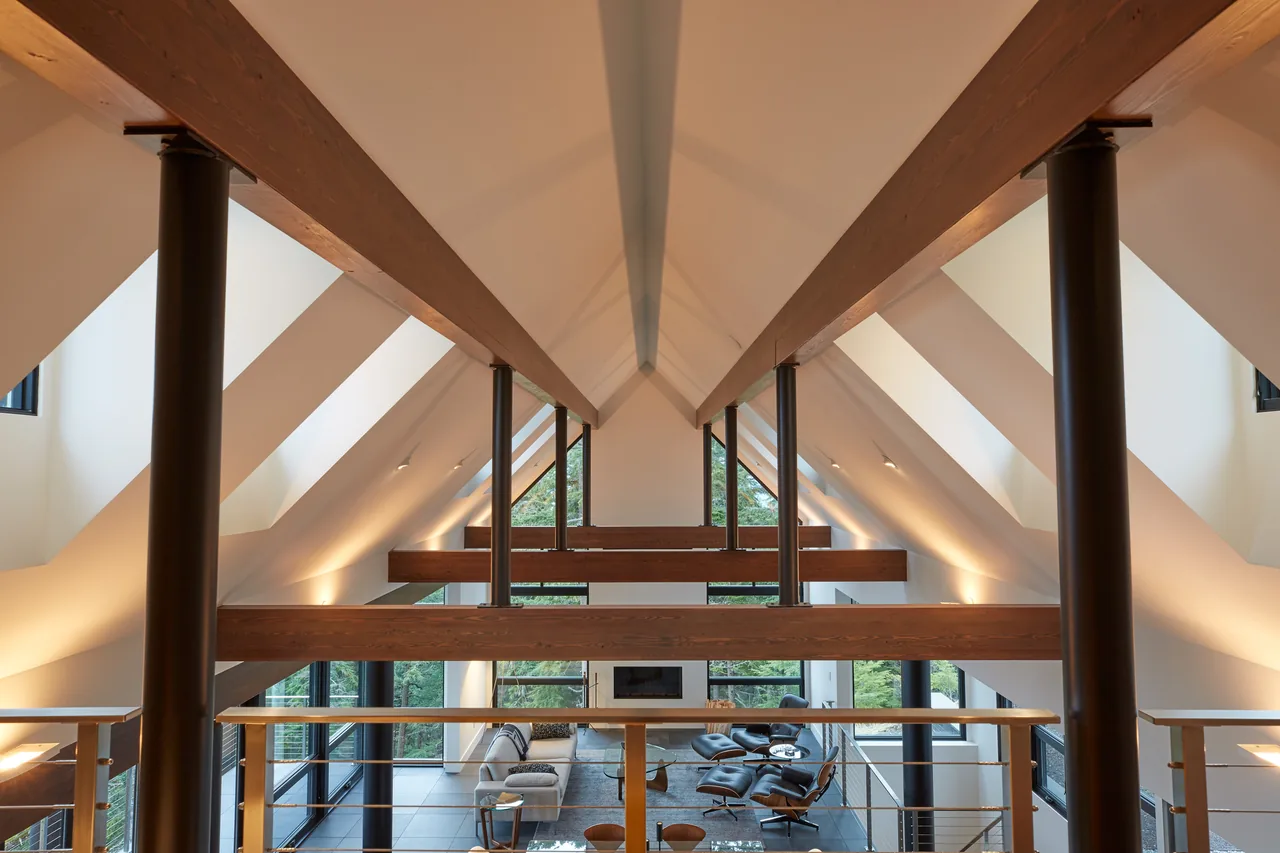 Vaulted ceiling living room with exposed wood beams and large glass windows overlooking a forested hillside.