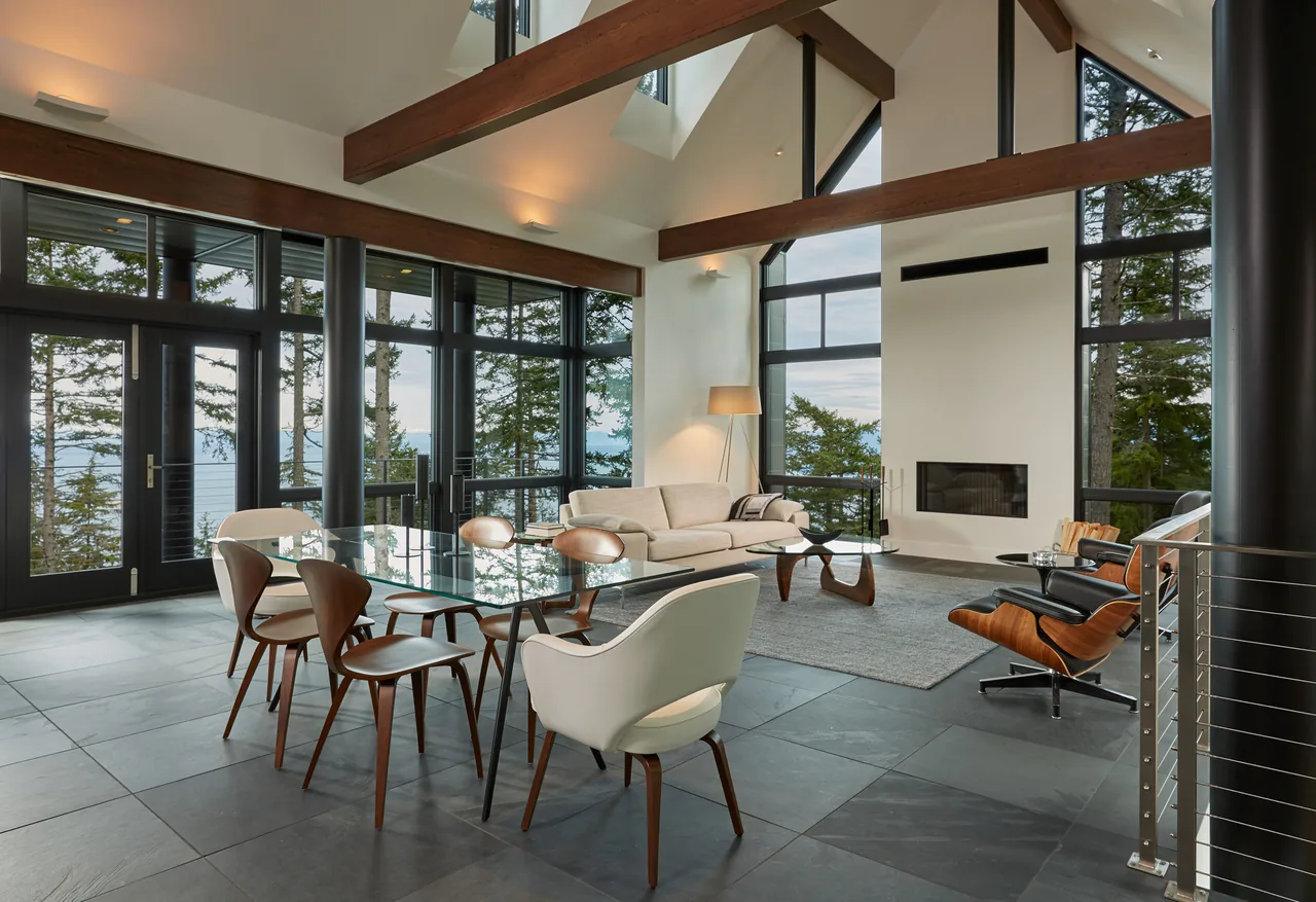 Modern living and dining space featuring floor-to-ceiling windows and exposed wood beams at Buck Mountain Residence.