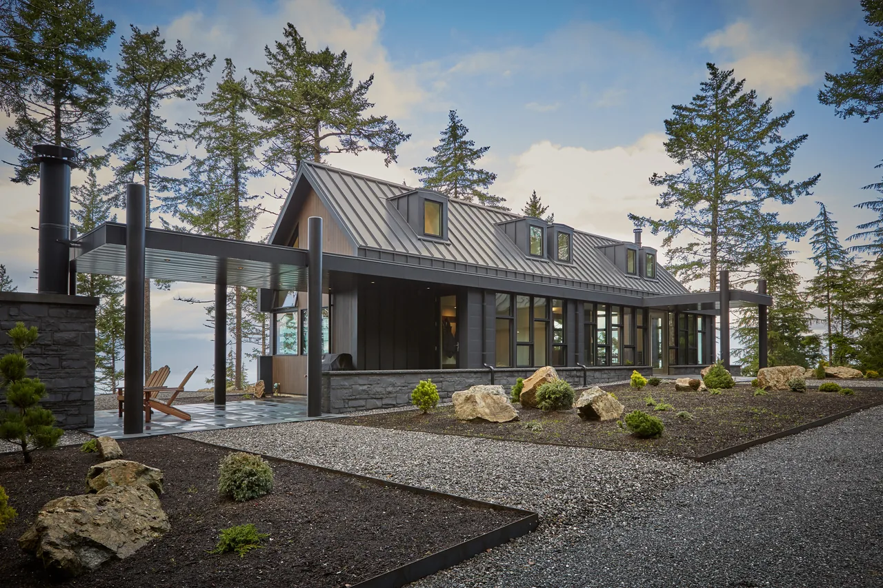 Buck Mountain Residence features a modern exterior with a standing seam metal roof and forest surroundings.