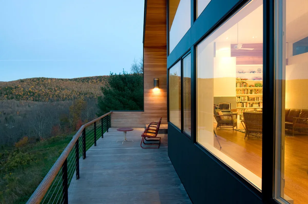 Large deck on hilltop house overlooking forested hills, with wood siding and black window frames.
