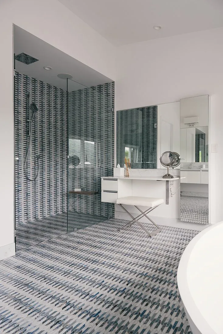 Bathroom features blue patterned tile on floor and shower walls with a floating white vanity and large mirror.