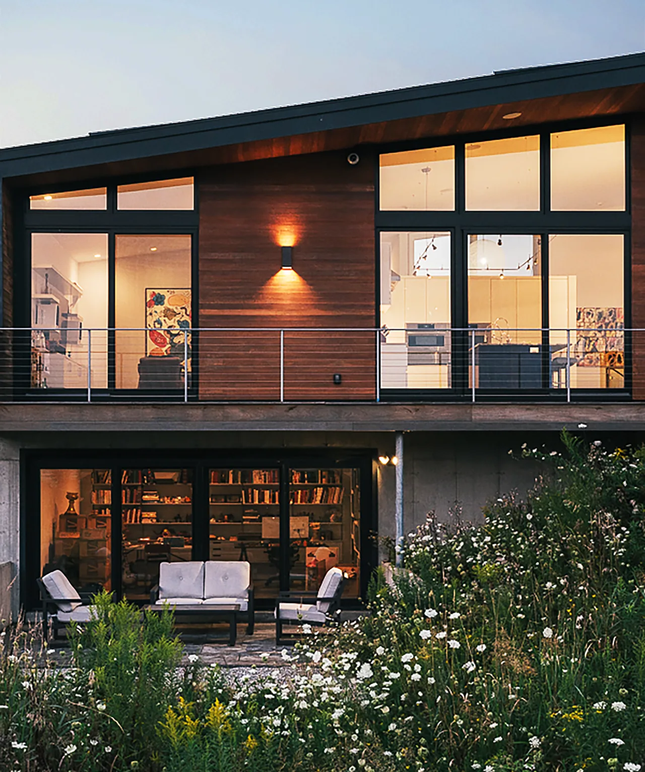 Rolling meadow house features wood siding, large black window frames, and outdoor seating, showcasing modern residential architecture.