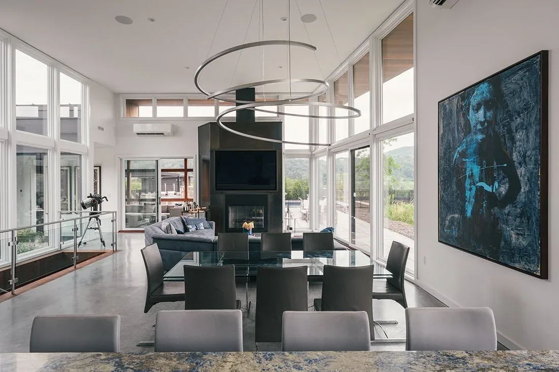 Open dining and living space features floor-to-ceiling glazing with black framed windows and a central dark fireplace.