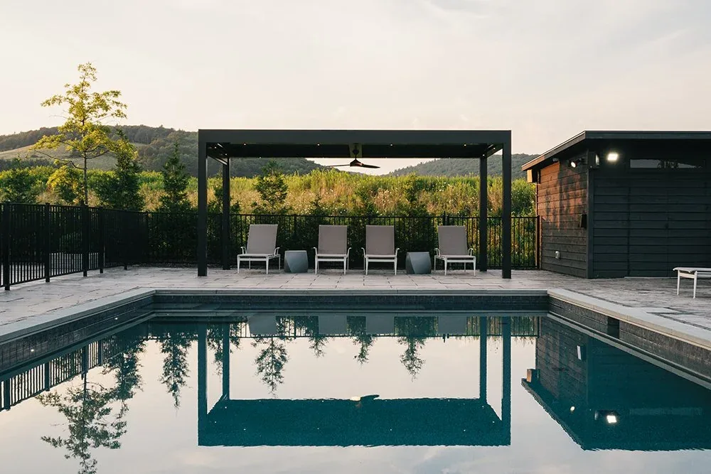 The Rolling meadow house features an outdoor pool area with a black pergola, lounge seating, and a pool house with wood siding.