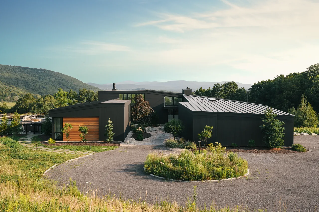 Rolling Meadow House by David Weiner Architects features dark exterior cladding, flat and standing seam metal roofs, and a circular driveway.