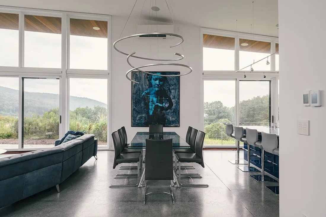 Dining space with floor-to-ceiling windows and black chairs around a glass table in the Rolling meadow house.