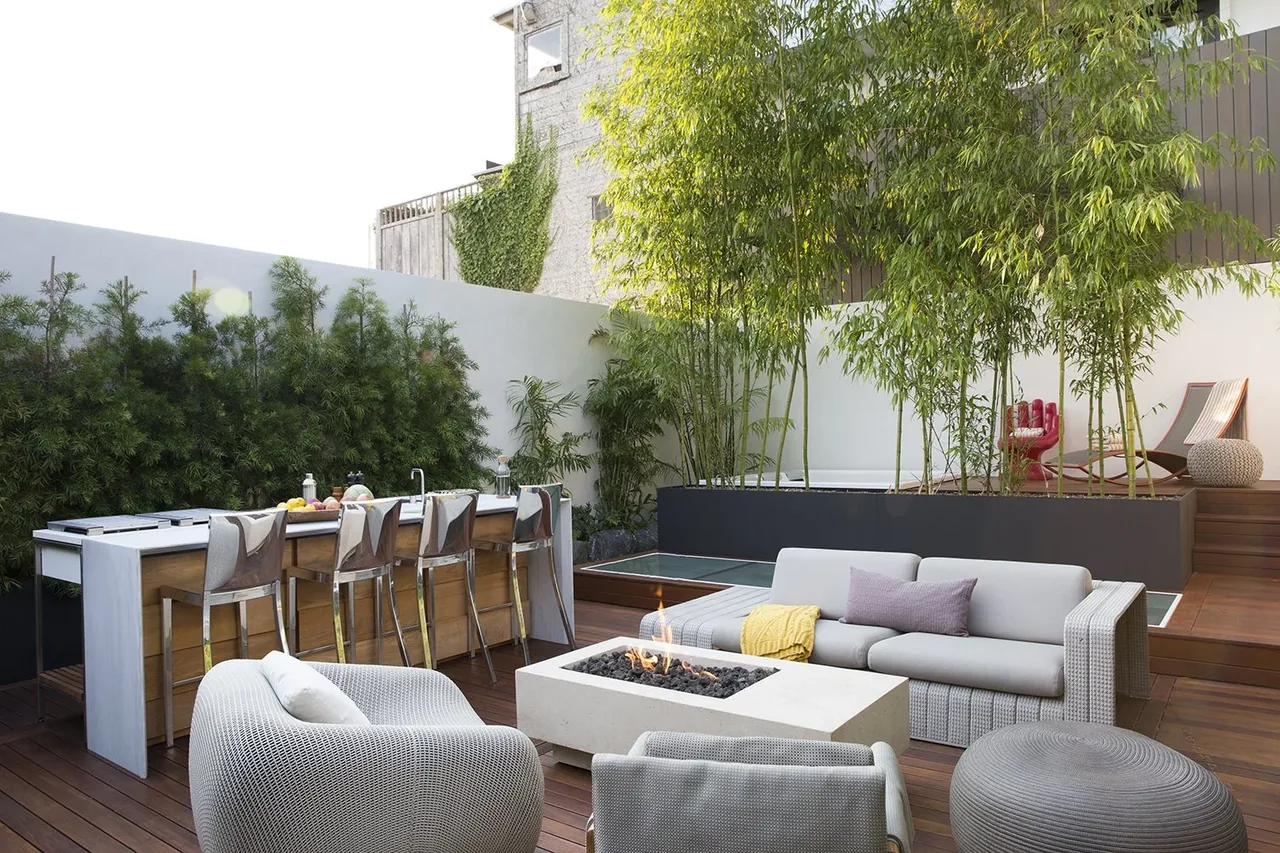 Modern outdoor living area featuring a fire pit, lounge seating, bar counter, and a raised bamboo planter, designed by Dawson & Clinton.