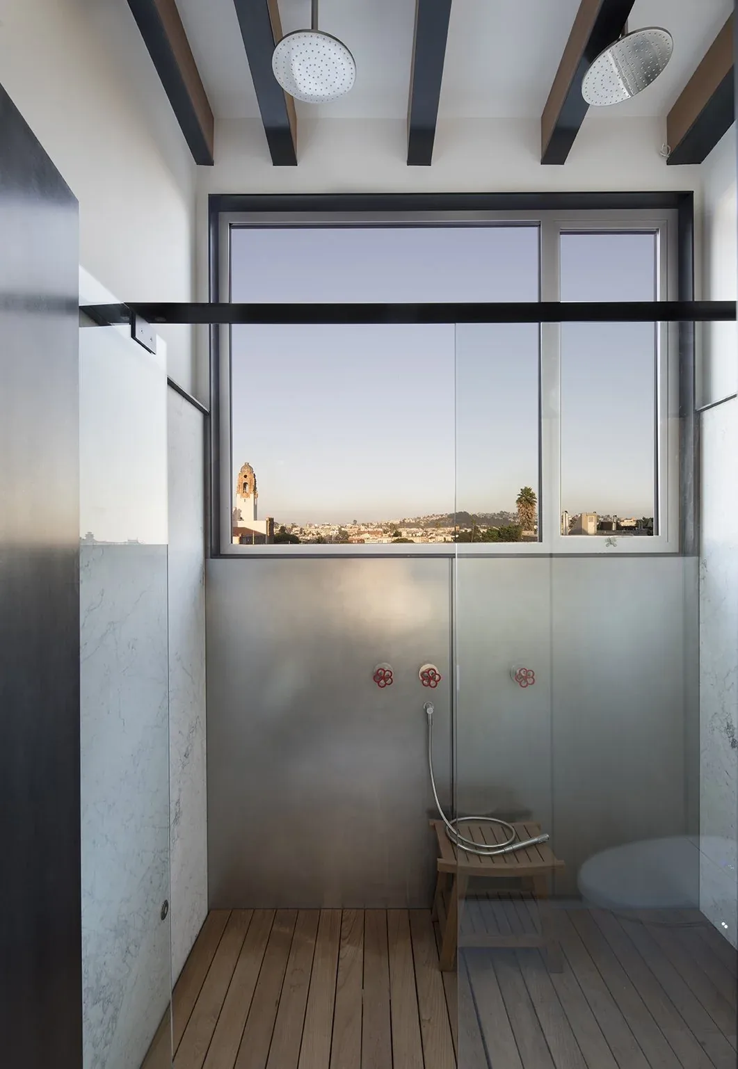Bathroom shower with wood flooring, metal wall, and two overhead rainfall showerheads overlooking cityscape.
