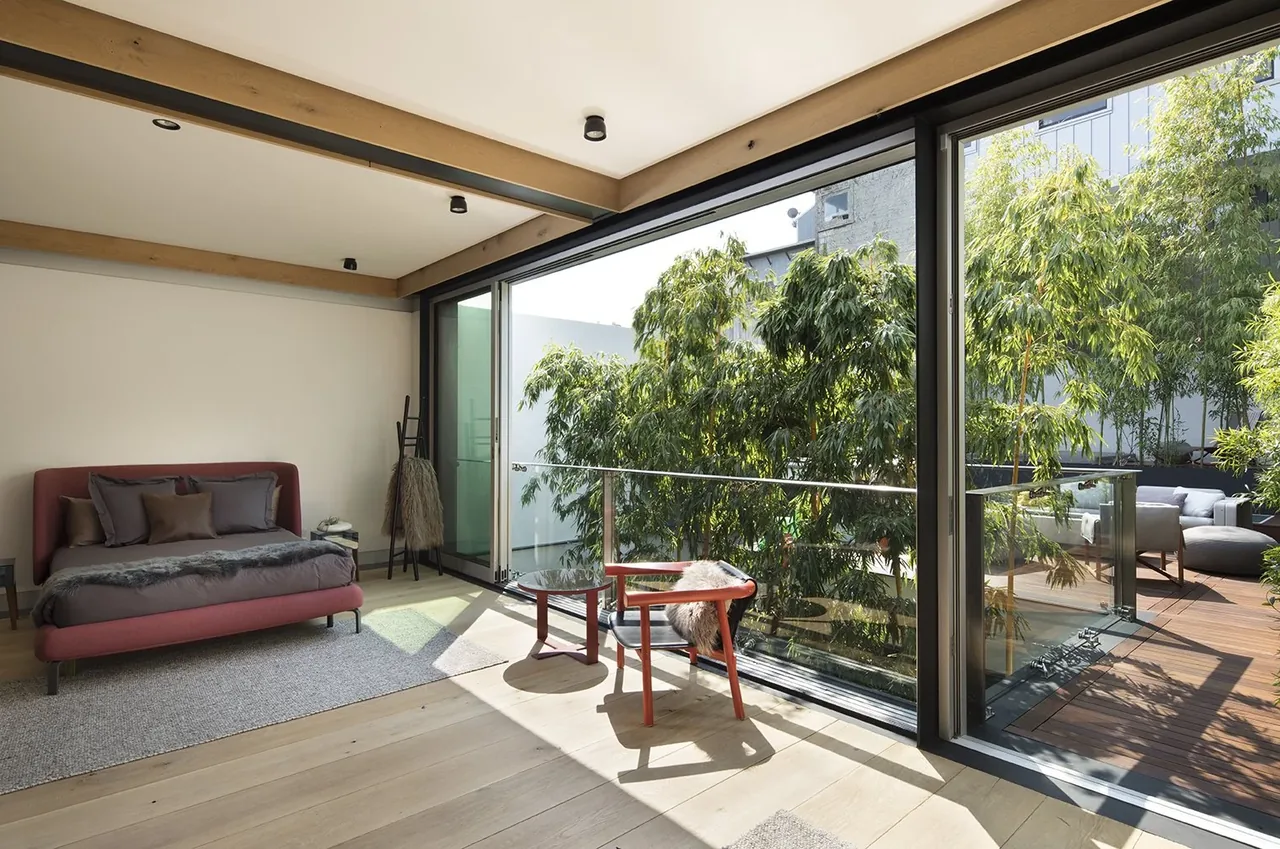 Bedroom featuring floor-to-ceiling glazing and a balcony with glass railing overlooking greenery.