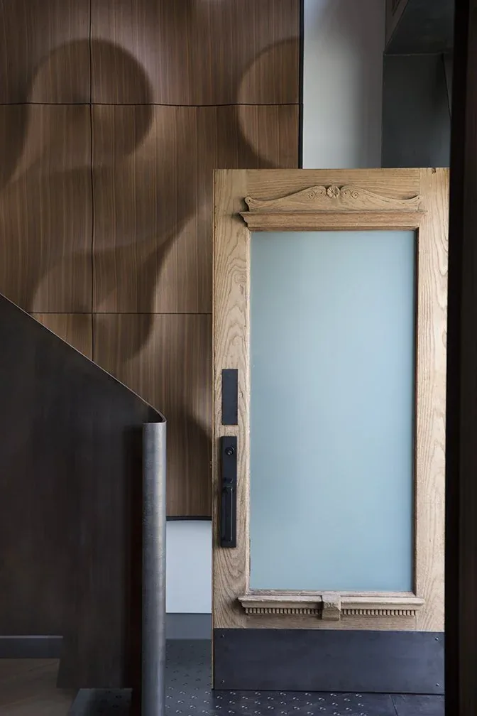 Interior view showing a wood-framed frosted glass door with decorative top trim beside a metal staircase and wood-paneled wall.