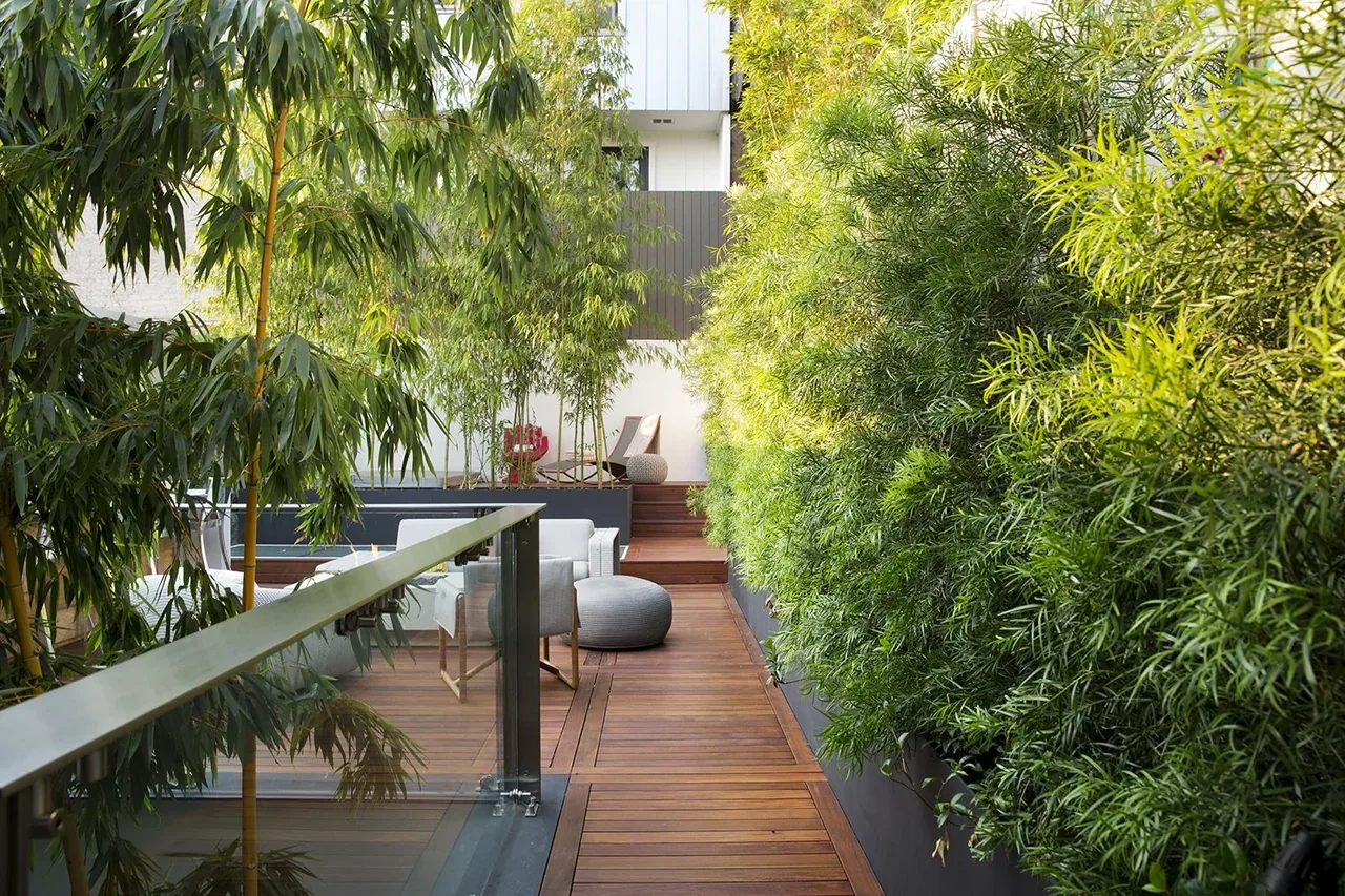 Wood-slat outdoor living deck with glass balcony railing and abundant greenery planters.