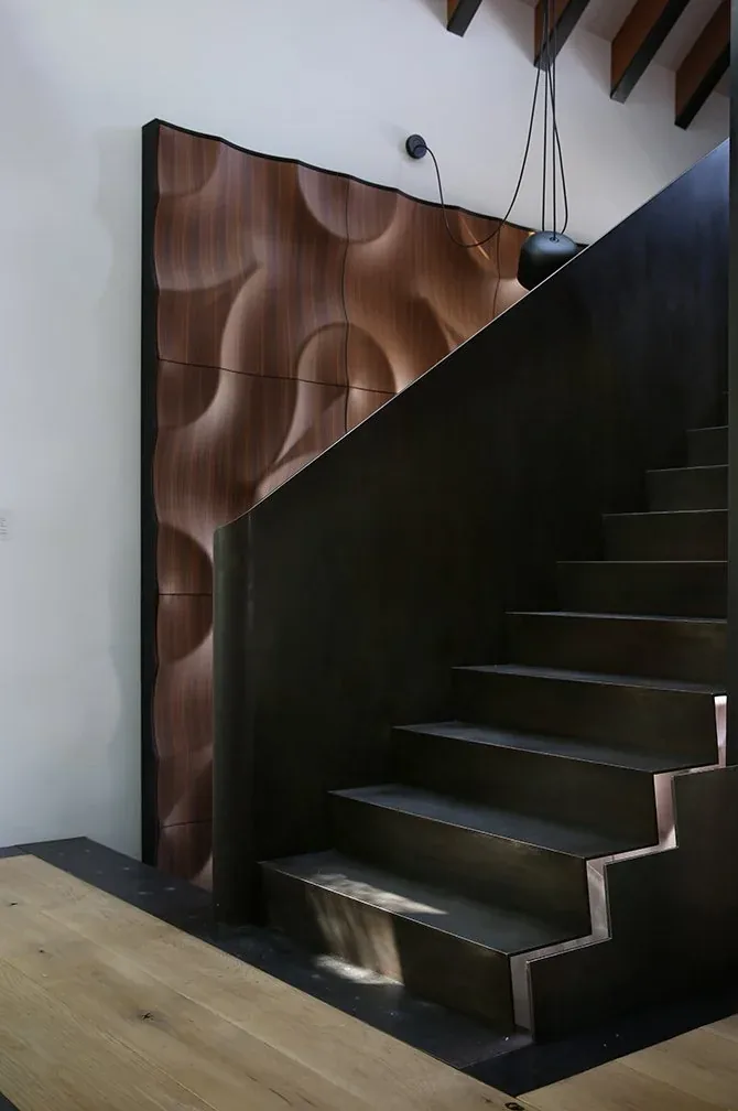 A modern black metal staircase is set against a sculpted wood wall panel with curved patterns in this interior.